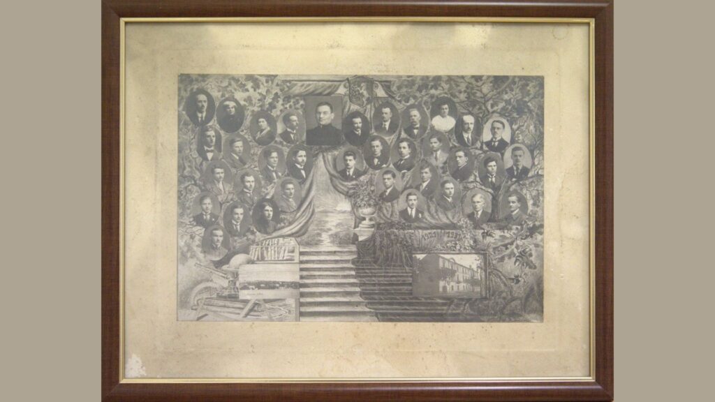 Zdjęcie złożone z wielu owalnych portretów na tle symbolicznego drzewa genealogicznego, którego pień przypomina schody. Na górze centralny portret mężczyzny w sutannie (prawdopodobnie dyrektor lub ksiądz), nad nim herb z orłem. Po lewej stronie widoczne są książki, mapy i przybory geometryczne. W prawym dolnym rogu zdjęcie budynku szkoły. Kolorystyka sepiowa, rama drewniana.