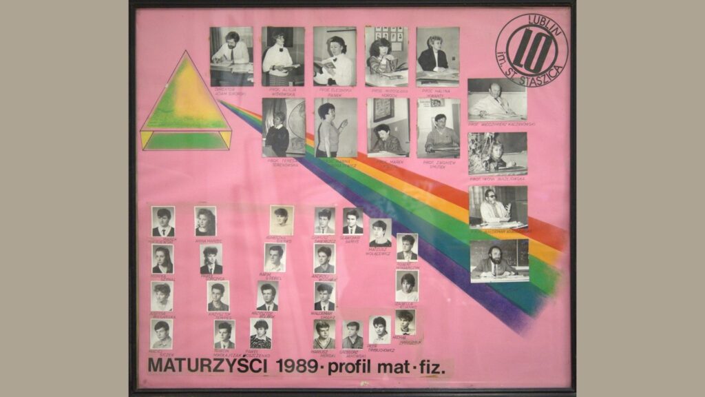 Plansza w kolorze różowym, z dużą kolorową tęczą promieniującą z zielono-żółtej piramidy w lewo. Na górze – 12 zdjęć nauczycieli w czasie zajęć (przy tablicy, biurku, z uczniami). Na dole – 30 czarno-białych zdjęć uczniów w prostokątnych ramkach, podpisanych imieniem i nazwiskiem. Napis: „Maturzyści 1989 – profil mat-fiz” w kolorze czarnym, wyśrodkowany na dole.