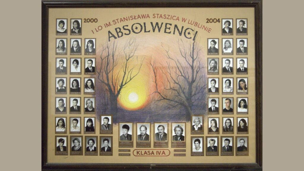 Tło w odcieniu beżowym z kolorowym rysunkiem pejzażu. W centrum znajduje się duże słońce wschodzące lub zachodzące za drzewami bez liści, na tle nieba w barwach od żółci, przez pomarańcz i fiolet po granat. U góry napis: „I LO im. Stanisława Staszica w Lublinie – ABSOLWENCI”, a po bokach lata „2000” i „2004”. Zdjęcia uczniów rozmieszczone są po lewej i prawej stronie ilustracji – w pionowych rzędach po 5 zdjęć w każdej kolumnie. Portrety czarno-białe, w brązowych ramkach, podpisane. Na dole – zdjęcia kadry pedagogicznej oraz podpis: „KLASA IVA” na tle czerwonego paska.