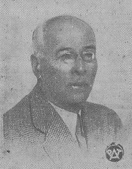 Ziarnista, czarno-biała fotografia Adama Szelągowskiego – starszego mężczyzny o łagodnym, ale czujnym spojrzeniu. Ma krótkie, siwiejące włosy i nosi garnitur z jasną koszulą. Jego twarz jest częściowo zacieniona. W dolnym prawym rogu widoczny jest emblemat organizacyjny, prawdopodobnie związany z działalnością społeczną lub polityczną. Styl zdjęcia sugeruje wczesne lata XX wieku, wykonane najpewniej do publikacji biograficznej lub archiwalnej.