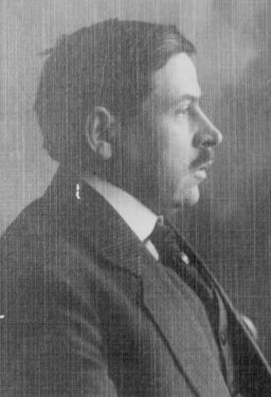 Rysunkowy portret mężczyzny o wyraźnie zaznaczonych rysach twarzy. Ma krótkie włosy i bokobrody, ubrany jest w ciemny surdut z wysokim kołnierzem. Styl ilustracji przypomina litografię z XIX wieku, portret ma charakter oficjalny, z lekko uniesionym spojrzeniem.