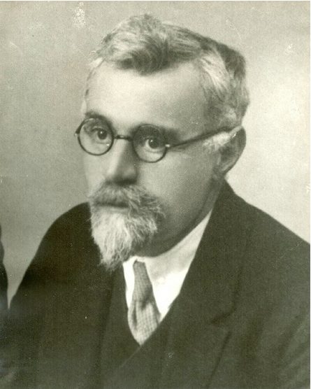 Czarno-biała fotografia mężczyzny w podeszłym wieku Jan Riabinin. Głowa całkowicie łysa, twarz z profilu. Ubrany w ciemny garnitur, białą koszulę i krawat. Mimika spokojna, dostojna. Zdjęcie prawdopodobnie z lat 30. lub 40. XX wieku, z miękkim światłem i klasycznym, studyjnym kadrem.