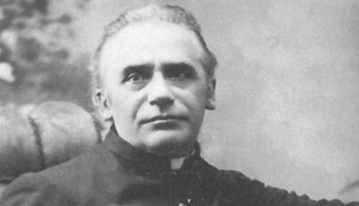 Czarno-białe zdjęcie księdza Józefa Dąbrowskiego w średnim wieku. Duchowny siedzi, ubrany w sutannę, patrzy spokojnie przed siebie. Włosy krótkie, siwiejące, rysy twarzy wyraźne. Zdjęcie wykonane w klasycznym stylu studyjnym z miękkim światłem.