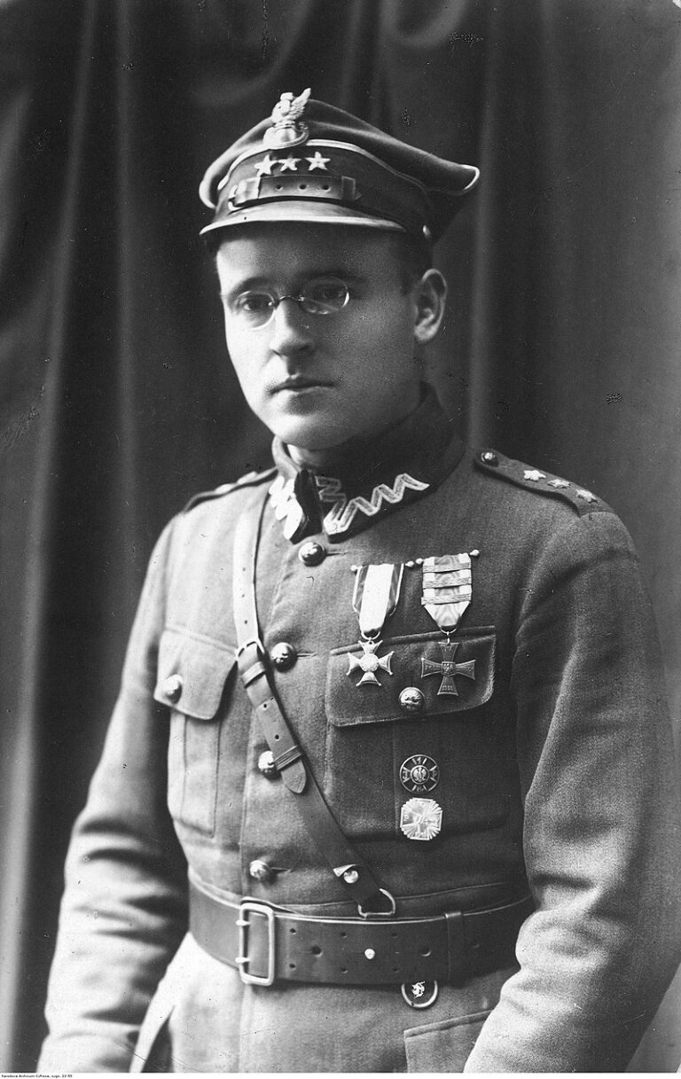 Czarno-biała fotografia przedstawia młodego mężczyznę w mundurze oficera Wojska Polskiego z okresu międzywojennego. Na głowie ma rogatywkę z orłem i trzema gwiazdkami, świadczącymi o stopniu oficerskim. Mężczyzna nosi okulary, patrzy na wprost i ma poważny wyraz twarzy. Mundur zdobią liczne ordery i odznaczenia, w tym Krzyż Walecznych i inne medale bojowe. Na piersi widoczna jest także skórzana szelka od pasa noszonego przez ramię. Tło stanowi zasłona – zdjęcie wykonano w atelier fotograficznym.