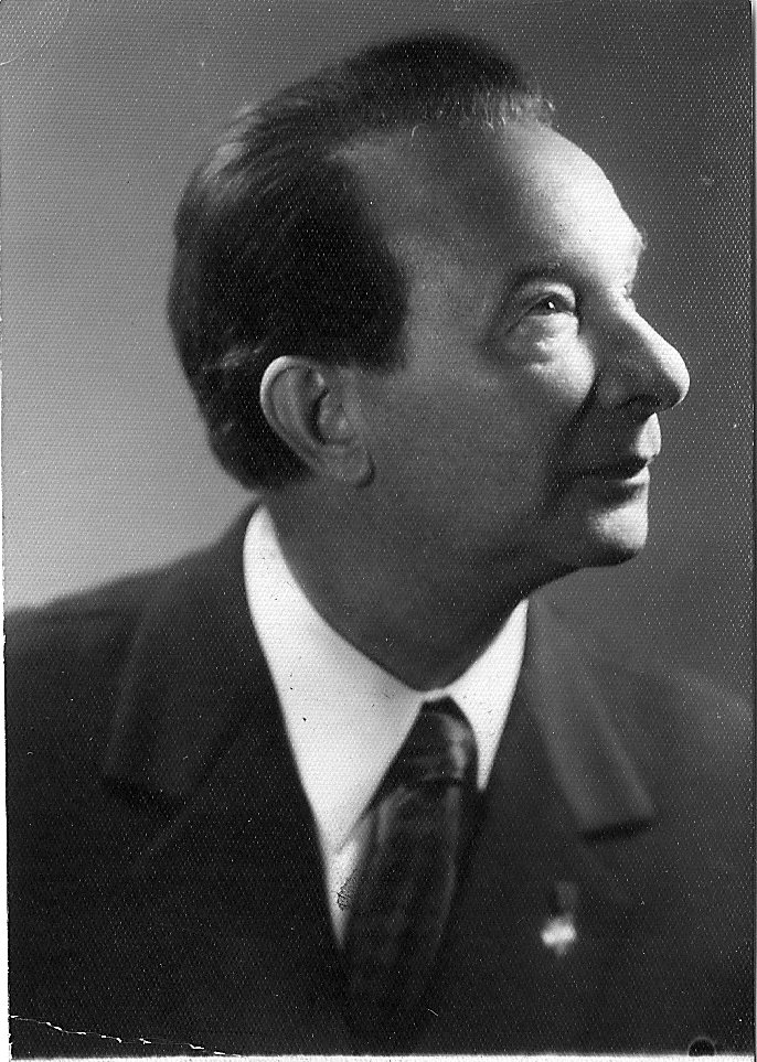 Czarno-biała fotografia Stefana Wolskiego – mężczyzny w średnim wieku, ukazanego z profilu. Ma gładko zaczesane włosy i nosi garnitur z szerokim krawatem. Spojrzenie skierowane ku górze, wyraz twarzy zadumany lub marzycielski. Tło neutralne, portret formalny, prawdopodobnie z połowy XX wieku.