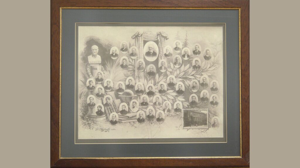 Typ obiektu: Stare, czarno-białe zdjęcie zbiorowe (fotomontaż) oprawione w ramkę. Przedstawia grupę osób – najprawdopodobniej nauczycieli i absolwentów szkoły z początku XX wieku. Zdjęcie wykonane w stylu pamiątkowego kolażu. Opis ogólny: Fotografia oprawiona jest w drewnianą ramę o ciemnym, brązowym kolorze z delikatnym złoconym wewnętrznym obrzeżem. Sama fotografia znajduje się na jasnym tle z dodatkową ciemnoszarą, kartonową oprawą wewnętrzną, która tworzy eleganckie passe-partout. Kompozycja zdjęcia: Na środku znajduje się duży owalny portret mężczyzny – prawdopodobnie dyrektora szkoły lub zasłużonego pedagoga – zawieszony na szarfie dekoracyjnej, opleciony liśćmi laurowymi. Bezpośrednio pod nim rozmieszczone są dziesiątki owalnych portretów osób – głównie mężczyzn, ale także kobiet. Wszystkie osoby ubrane są bardzo elegancko, w garnitury, suknie, niektóre z odznakami lub oznaczeniami funkcji. Portrety ułożone są w symetryczny sposób, w gęstym układzie o kształcie elipsy lub wachlarza, oplecione dekoracyjną grafiką z motywami liści, książek, globusa i przyborów naukowych. W lewym górnym rogu znajduje się popiersie starszego mężczyzny na postumencie. Na cokole widoczny jest napis: „S. Staszic 1910” – co sugeruje, że może to być popiersie Stanisława Staszica, patrona szkoły. W prawym dolnym rogu znajduje się miniatura zdjęcia budynku szkolnego – prawdopodobnie front szkoły, z podpisem pod spodem i małym portretem. U dołu zdjęcia można zauważyć podpis autora lub wykonawcy montażu fotograficznego: „Zakład Artystyczno-Fotograficzny Lublin”. Elementy graficzne i symboliczne: Tło zdjęcia jest ilustrowane ozdobnymi liśćmi laurowymi – symbolem wiedzy, nauki i zwycięstwa. Pośród portretów znajdują się symbole nauki: książki, globus, cyrkiel, laska geometryczna – sugerujące edukacyjny charakter instytucji. Użyty styl graficzny to typowa dla początku XX wieku forma portretów klasowych i jubileuszowych – każdy portret został oprawiony w delikatną, białą owalną ramkę, lekko wypukłą. Znaczenie: Obraz najprawdopodobniej upamiętnia rocznicę, zakończenie nauki, jubileusz szkoły lub jej grona pedagogicznego – może to być klasa maturalna lub absolwenci z roku 1910. Uczniowie i nauczyciele zostali przedstawieni z dbałością o hierarchię i detale. Kompozycja podkreśla powagę, wiedzę i prestiż miejsca, które reprezentują.