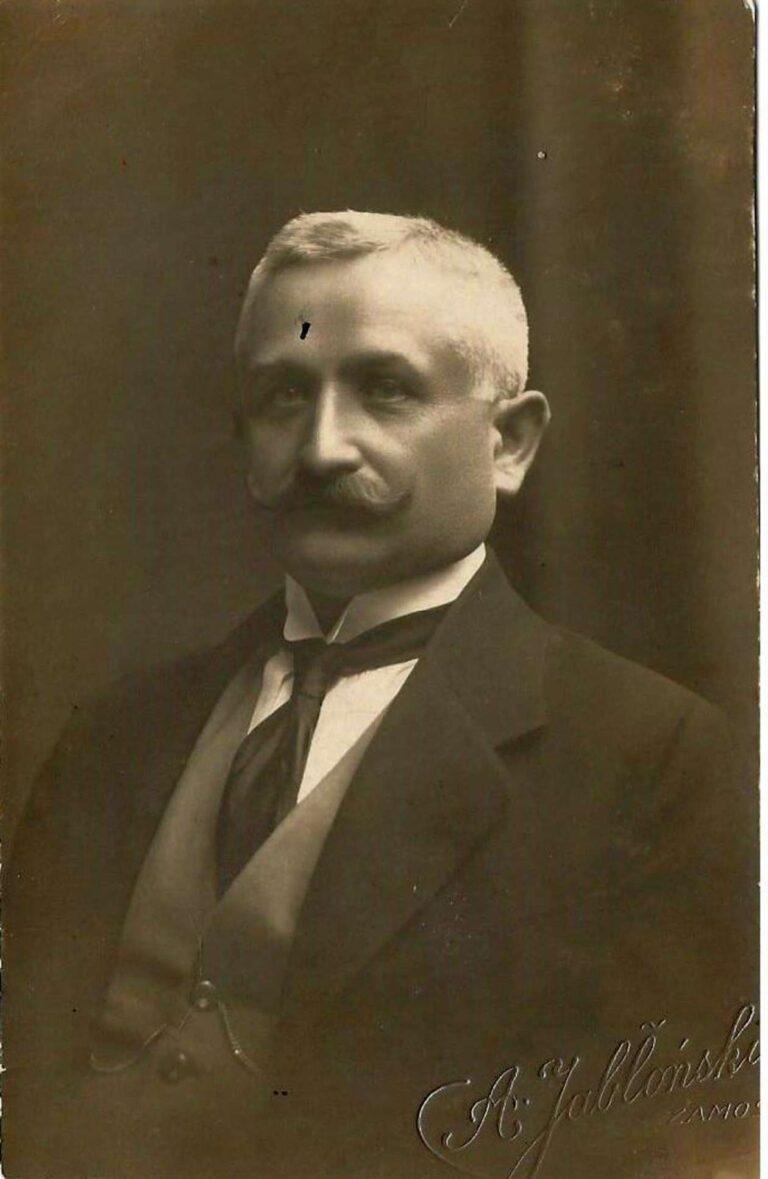 Czarno-białe, portretowe zdjęcie studyjne przedstawia starszego mężczyznę ( Wacława Bajkowskiego) w eleganckim stroju z początku XX wieku. Ma krótkie, siwe włosy i starannie ułożony, gęsty wąs podkręcony na końcach. Ubrany jest w ciemną marynarkę, jasną kamizelkę, białą koszulę i ciemny krawat przewiązany na kokardę. Na kamizelce widoczny jest łańcuszek od zegarka kieszonkowego. Tło jest jednolite i ciemne. W prawym dolnym rogu zdjęcia znajduje się podpis fotografa: „A. Jabłoński, Zamość”.