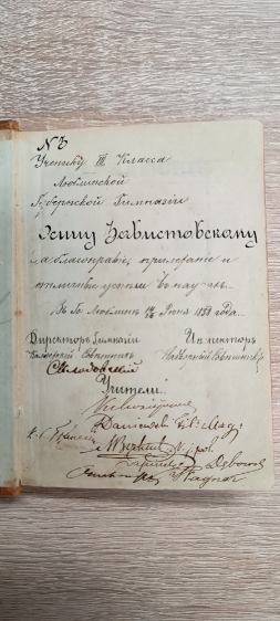 To zbliżenie prawej strony poprzedniego dokumentu, ukazujące dokładnie kaligraficzny tekst.
Litery są pisane dużymi, ozdobnymi pociągnięciami, typowymi dla dokumentów z XIX wieku.
Tekst w języku rosyjskim zawiera imię i nazwisko ucznia oraz informację o nagrodzie lub wyróżnieniu szkolnym.
Na dole znajduje się kilka podpisów oraz ozdobny znak graficzny przypominający podpis dyrektora. Papier ma lekko żółty odcień, a przy grzbiecie widać ślady zszycia nicią.