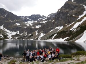Wyprawa górska – wielka grupa nad jeziorem w górach (widok panoramiczny).