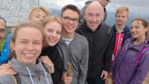 Selfie grupowe na wycieczce w terenie, w tle góry/mapa.