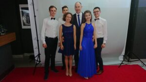 Wydarzenie szkolne/studniówkowe – grupa elegancko ubranych osób na tle ścianki.