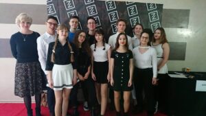 Wydarzenie szkolne – grupa elegancko ubranych osób na tle ścianki.