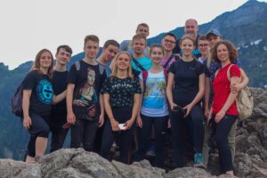 Wycieczka w góry – grupa młodzieży na skałach, w tle górski krajobraz.