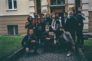 Grupa uczniów przed budynkiem szkoły, większość w maseczkach, trzymają teczki/świadectwa.