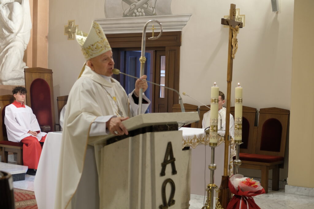 Biskup w białych szatach liturgicznych przemawia w kościele.