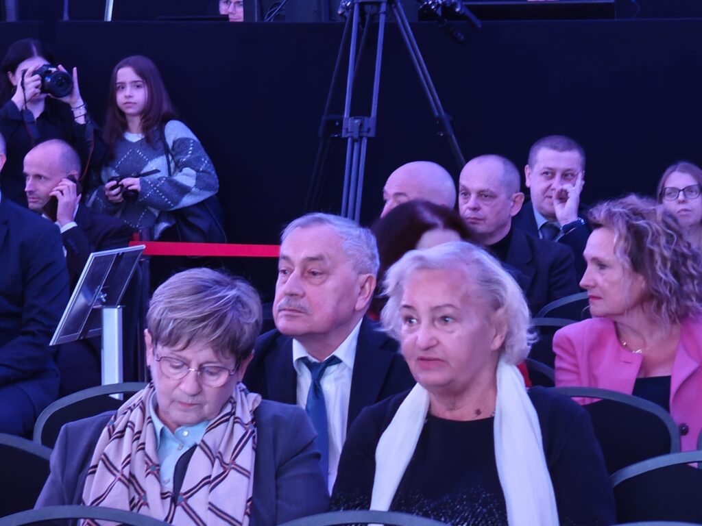 Publiczność uczestniczy w wydarzeniu odbywającym się przy kolorowym oświetleniu.