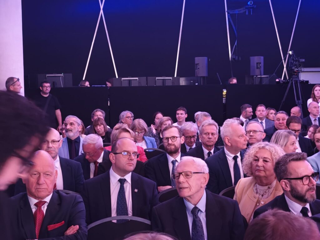 Elegancko ubrani goście siedzą podczas oficjalnej uroczystości.