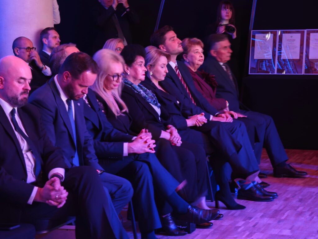 Publiczność ogląda wydarzenie w sali oświetlonej na niebiesko.