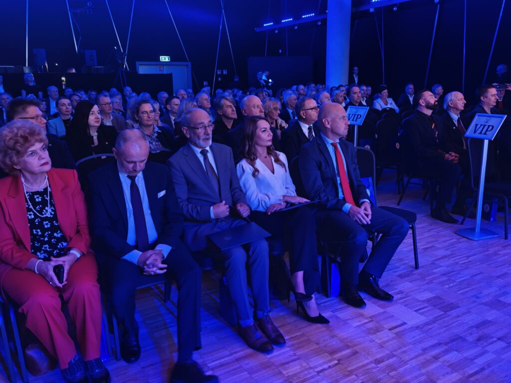 Publiczność ogląda wydarzenie w sali oświetlonej na niebiesko.