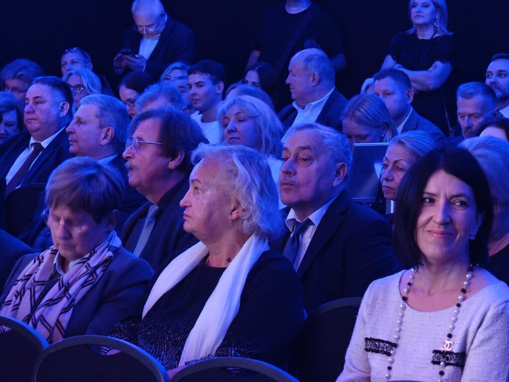 Publiczność ogląda wydarzenie w sali oświetlonej na niebiesko.