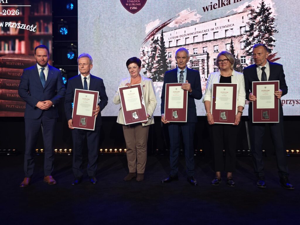Cztery osoby prezentują oprawione dyplomy podczas jubileuszowej uroczystości.