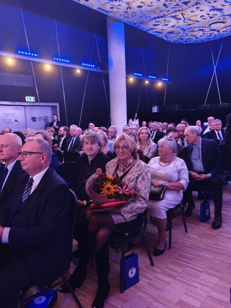 Publiczność siedzi w rzędach krzeseł podczas jubileuszowego wydarzenia.