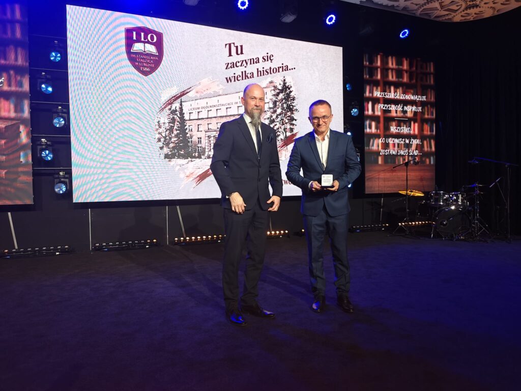Dwaj mężczyźni w garniturach stoją na scenie podczas jubileuszowej uroczystości.
