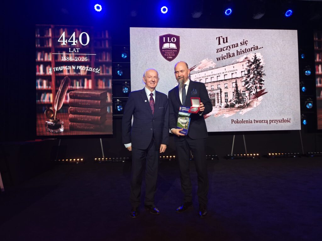 Dwaj mężczyźni w garniturach stoją na scenie podczas jubileuszowej uroczystości.