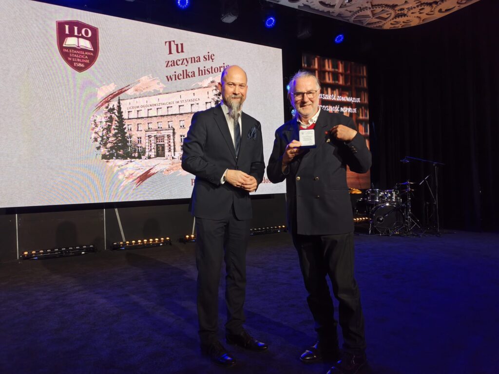 Dwaj mężczyźni rozmawiają na scenie, jeden trzyma mikrofon