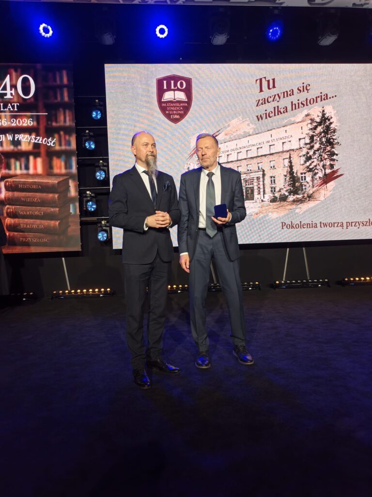 Dwaj mężczyźni w garniturach stoją na scenie podczas jubileuszowej uroczystości.