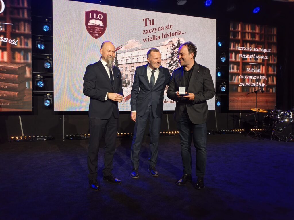 Trzy osoby stoją na scenie podczas wręczania jubileuszowych wyróżnień.