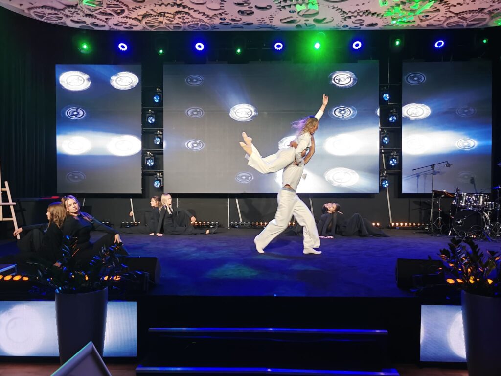 Artysta w jasnym stroju wykonuje dynamiczny taniec na scenie.