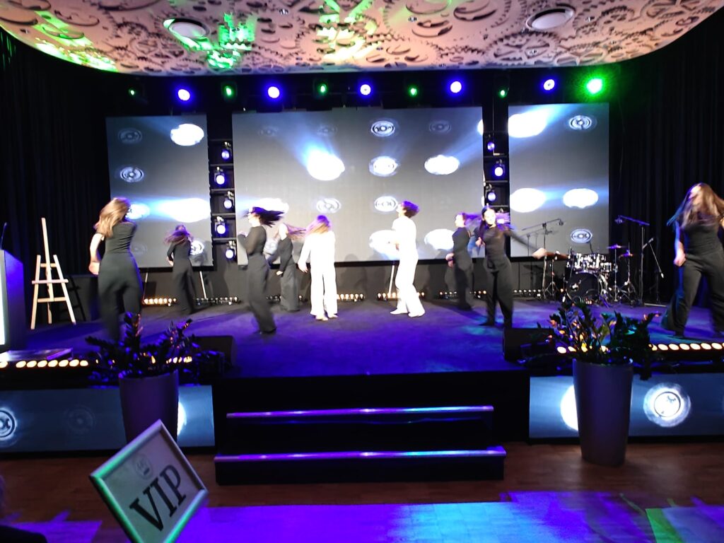 Zespół muzyczny występuje na scenie w świetle zielonych i niebieskich reflektorów.