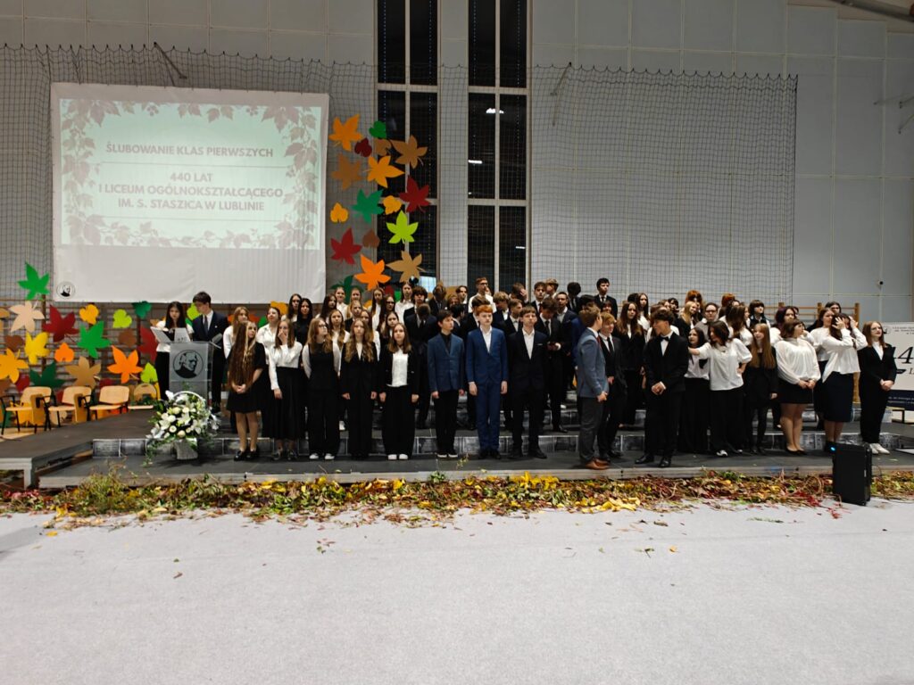 Liczna grupa uczestników uroczystości pozuje do wspólnego zdjęcia w sali gimnastycznej.