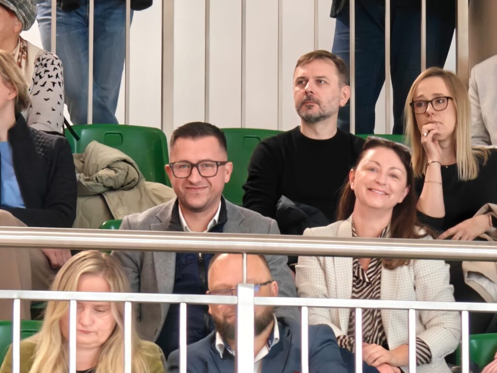 Kilka osób uśmiecha się do zdjęcia zza barierki na szkolnej sali.