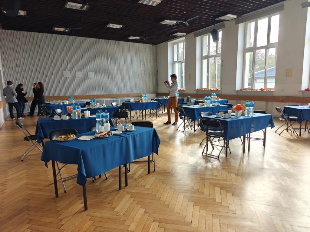 Sala przygotowana na przyjęcie gości, ze stołami nakrytymi niebieskimi obrusami.