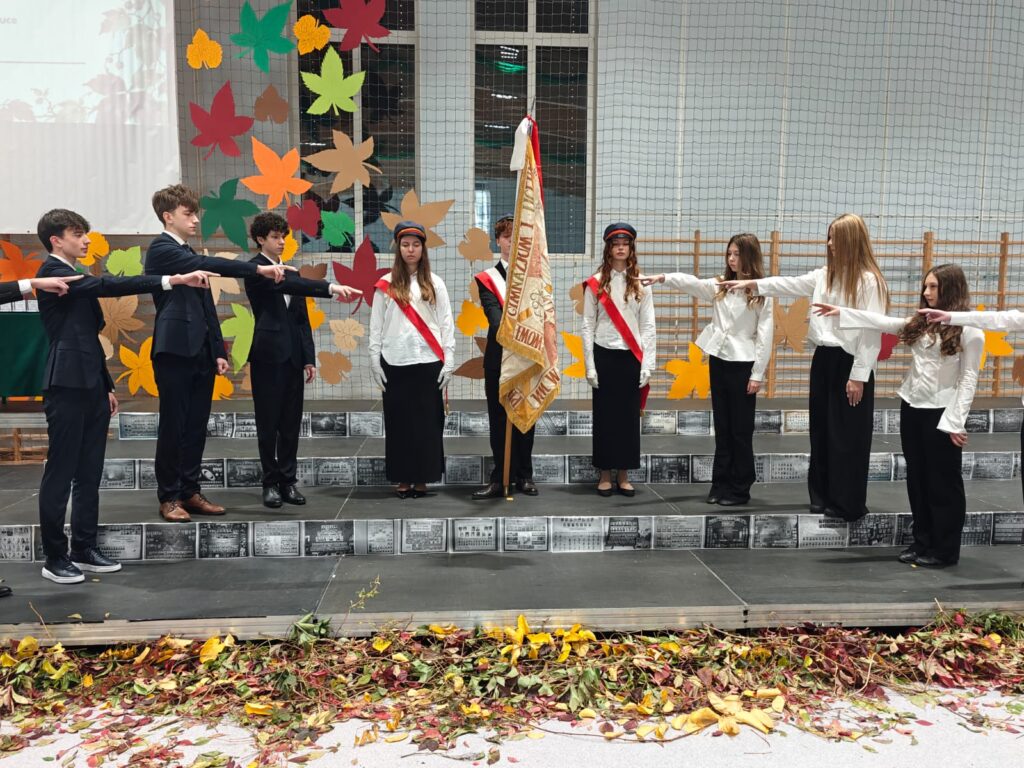 Poczet sztandarowy i uczniowie uczestniczą w uroczystej ceremonii szkolnej.