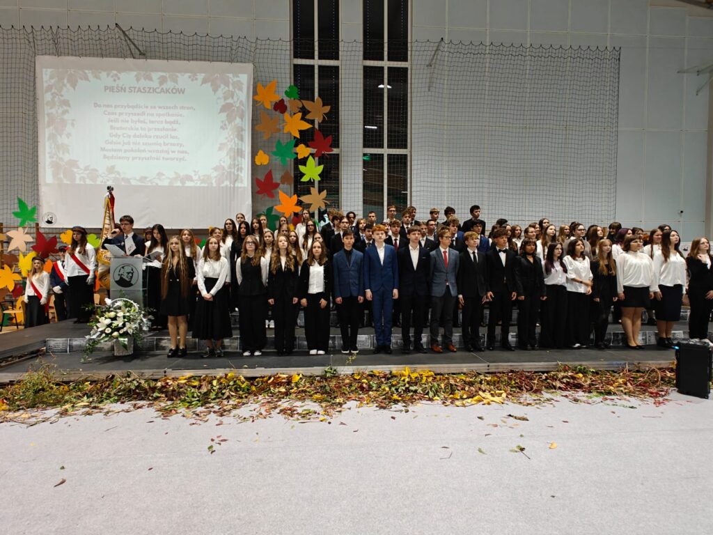 Liczna grupa uczestników uroczystości pozuje do wspólnego zdjęcia w sali gimnastycznej.