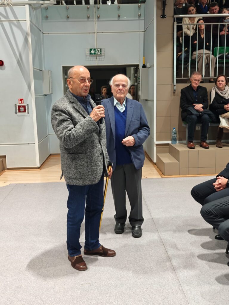 Mężczyzna z mikrofonem przemawia do zgromadzonych gości, obok stoi drugi mężczyzna.