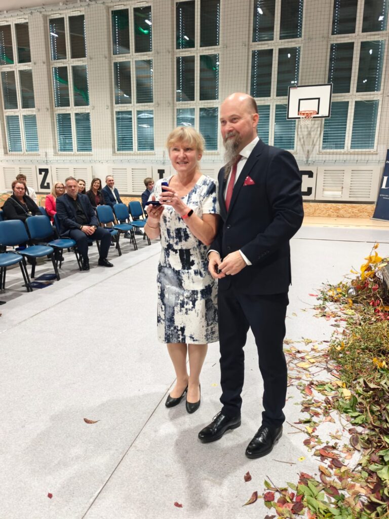 Kobieta w kwiecistej sukience przemawia przez mikrofon obok mężczyzny w garniturze.