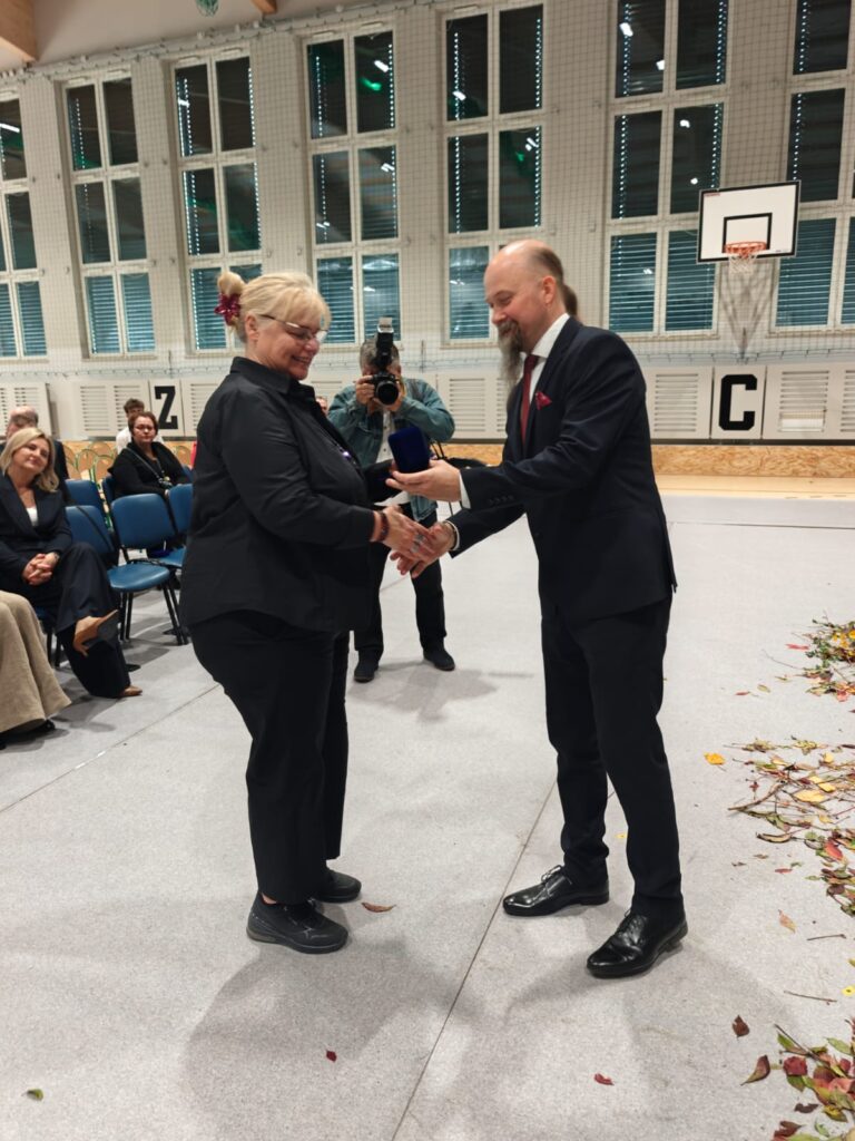 Mężczyzna przekazuje upominek kobiecie w ciemnym stroju.