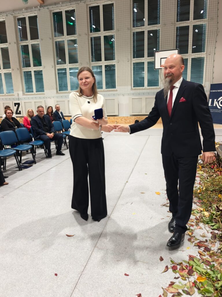 Mężczyzna wręcza dokument młodej kobiecie w białej bluzce.
