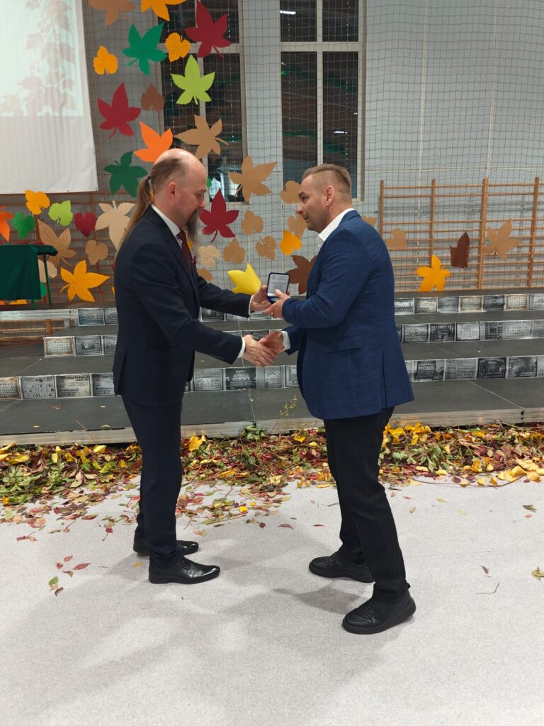 Dwaj mężczyźni wymieniają uścisk dłoni podczas wręczania wyróżnienia.
