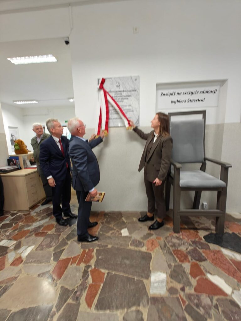 Uczestnicy uroczystości odsłaniają tablicę pamiątkową na ścianie szkolnego budynku.