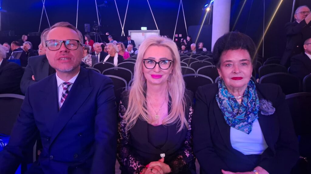 Trzy osoby pozują do wspólnego zdjęcia w sali widowiskowej.